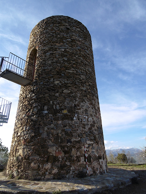 Una torre cilíndrica de piedra con una pequeña plataforma metálica elevada y un cielo azul con algunas nubes de fondo.

Descripción generada con IA
